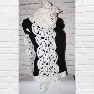 May include: White crocheted scarf with a delicate floral pattern. The scarf is long and flowing, with a scalloped edge.