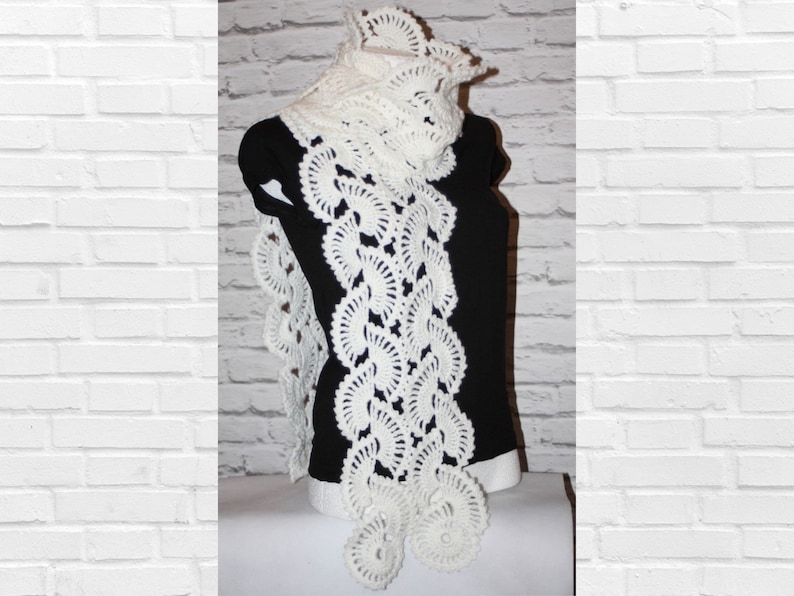 May include: White crocheted scarf with a delicate floral pattern. The scarf is long and flowing, with a scalloped edge.