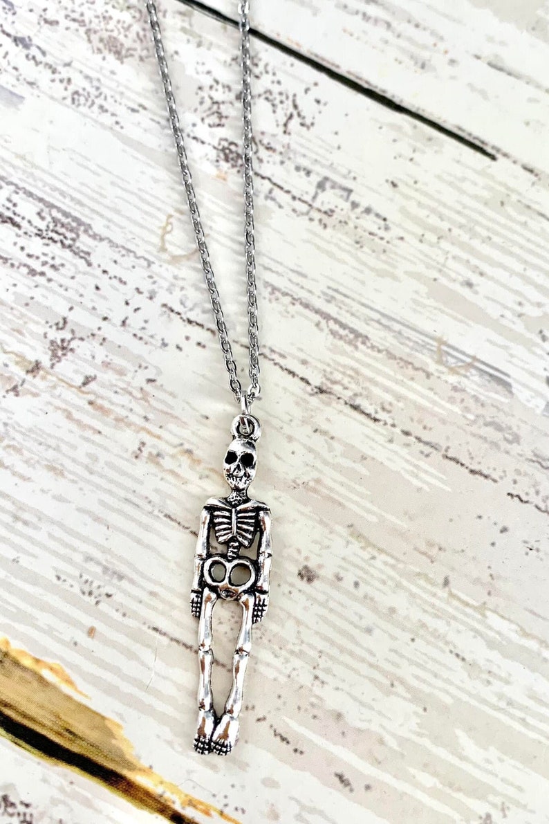 K&ouml;nnte beinhalten: Eine silberne Skelett-Anh&auml;ngerkette an einer silbernen Kette. Der Anh&auml;nger ist detailliert und zeigt einen Sch&auml;del und einen Brustkorb.