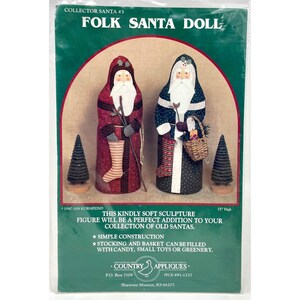 May include: A Folk Santa Doll kit with two Santa figures, one in red and one in blue, each holding a staff and stocking. The kit includes two small, dark green Christmas trees. The package text reads "Collector Santa #3" and "Folk Santa Doll."