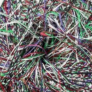 May include: A close-up of a tangled mass of colorful yarn. The yarn strands are a mix of colors, including green, red, white, black, and purple. The yarn appears to be made of a shiny, textured material, suitable for crafting projects.