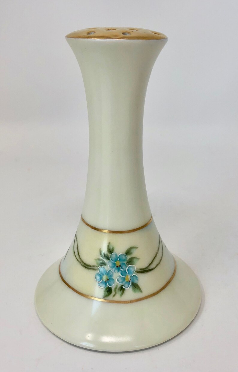 May include: A white ceramic flower frog with a gold rim and blue forget-me-not flowers painted on the base.