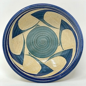 May include: A ceramic bowl with a blue rim and a decorative pattern. The bowl features a central teal circle surrounded by cream-colored shapes and dark blue accents, creating a spiral design.