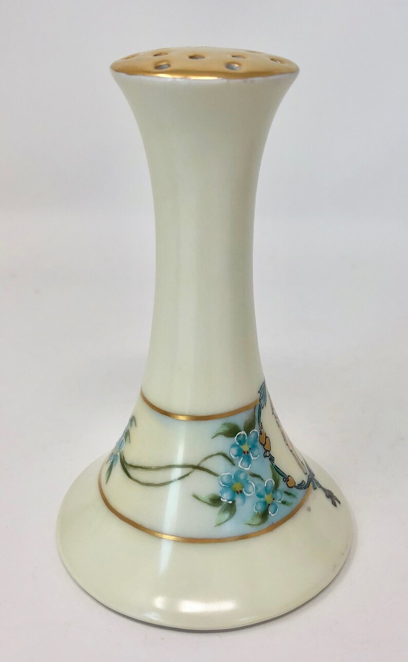 May include: A white ceramic flower frog with a gold rim and blue forget-me-not flowers painted on the base.