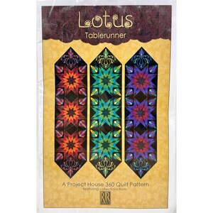 May include: A packaged table runner quilt pattern. The pattern features three vertical designs with starburst patterns in orange, green, and purple. The top of the package reads "Lotus Table Runner" in a decorative font. The bottom of the package reads "A Project House 360 Quilt Pattern".