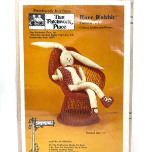 May include: A sewing pattern for a stuffed rabbit toy, titled "Rare Rabbit" by That Patchwork Place. The pattern shows a finished rabbit doll seated in a wicker chair. The finished size is 71 inches.