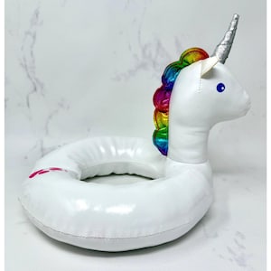 May include: A white inflatable unicorn pool float with a shiny finish. It features a metallic silver horn, a vibrant rainbow-colored mane, and a small blue eye. The circular base has a smooth texture with a small pink graphic detail on the side.