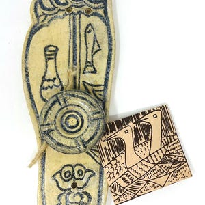 May include: A ceramic foot-shaped incense holder with blue and cream accents. The design includes a bottle, fish, and a circular incense holder. A small tag with bird illustrations is attached.