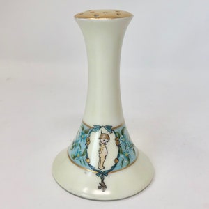 May include: White porcelain salt shaker with a blue and gold floral design and a small child figure in the center. The top of the shaker has a gold rim and holes for dispensing salt.