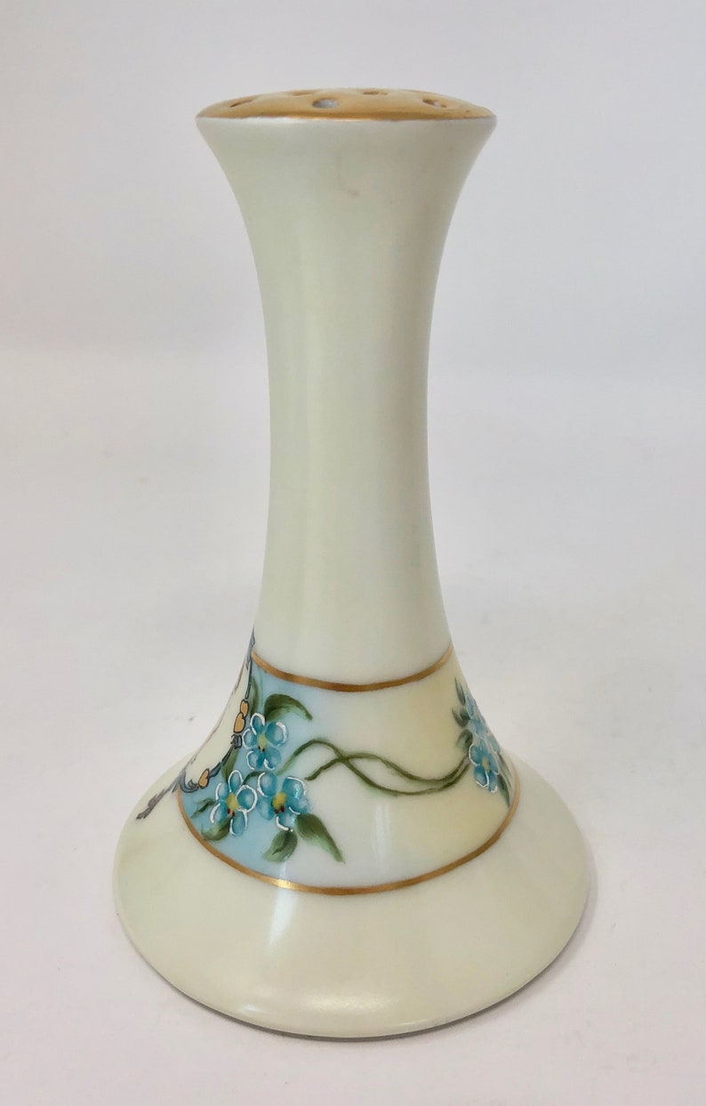 May include: A white porcelain vase with a gold rim and blue forget-me-not flowers painted on the side. The vase has a flared base and a narrow neck with holes for flower stems.