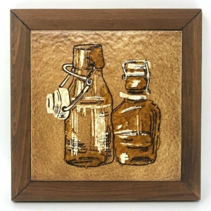 May include: Two brown glass bottles with wire closures on a brown tile background. The bottles are in a wooden frame.