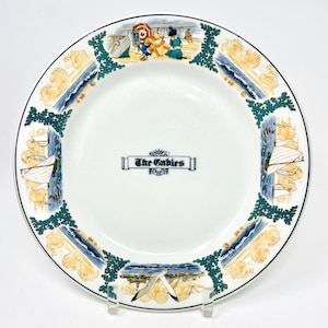 May include: White ceramic plate with a black rim, featuring a seaside design. The plate has illustrations of sailboats, beach scenes, and the text "The Gables" in the center. Decorative green and yellow accents surround the plate.