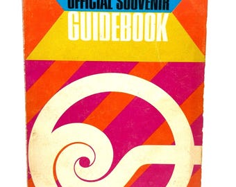 May include: A vintage guidebook cover with a colorful geometric design. The top section features blue, orange, and yellow shapes with the text "HEMISFAIR 1968 OFFICIAL SOUVENIR GUIDEBOOK." The lower half has diagonal orange and pink stripes with a white spiral design.