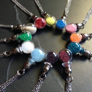 May include: A collection of glass vial necklaces filled with colorful glitter. Each vial is suspended from a silver chain. The glitter colors include white, red, yellow, blue, pink, green, orange, and purple.