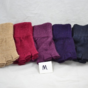May include: Five fingerless gloves in a row, each a different color. From left to right, the colors are tan, burgundy, purple, dark purple, and navy blue. The gloves are made of a knitted material and have a ribbed cuff.