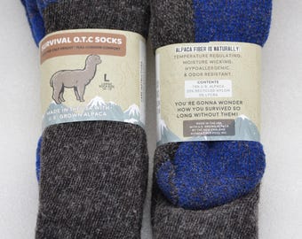 May include: Two pairs of grey and blue alpaca wool socks. The socks are labelled "Survival O.T.C Socks" and "Made in the USA with U.S. Grown Alpaca." The socks are large, with a calf height and full cushion comfort.