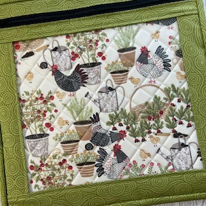 Pu&ograve; includere: Un pannello di tessuto trapuntato con un bordo verde e una cerniera nera. L'interno presenta un motivo ripetuto di polli, annaffiatoi, piante in vaso e bacche su uno sfondo color crema. Il bordo ha un design a spirale verde.