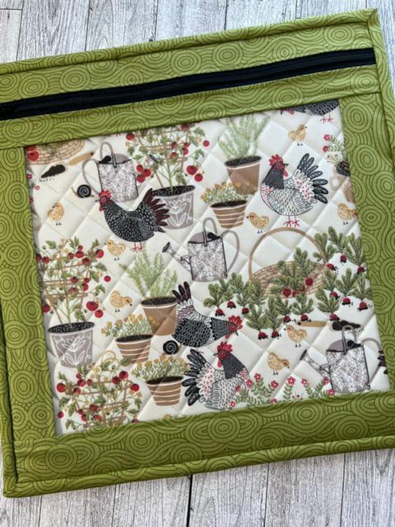 Pu&ograve; includere: Un pannello di tessuto trapuntato con un bordo verde e una cerniera nera. L'interno presenta un motivo ripetuto di polli, annaffiatoi, piante in vaso e bacche su uno sfondo color crema. Il bordo ha un design a spirale verde.