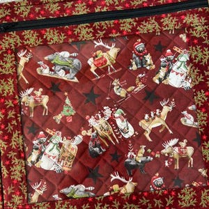 May include: A quilted fabric pouch featuring a dark red background with a repeating pattern of woodland animals, including bears, deer, and raccoons, wearing winter accessories. The pouch has a black zipper and a border with gold pine branches.