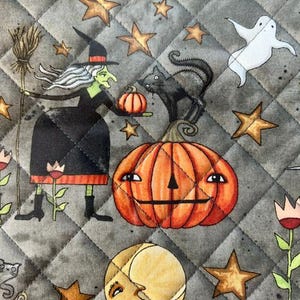 May include: A quilted fabric featuring a Halloween pattern on a gray background. The print includes a green-skinned witch holding a broom and pumpkin, a black cat, a large orange jack-o'-lantern, a white ghost, stars, and a crescent moon.