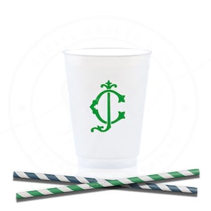 May include: A white plastic cup with a green monogram and two striped paper straws. One straw has green and white stripes, and the other has blue and white stripes. The cup is centered, and the straws are in the foreground.