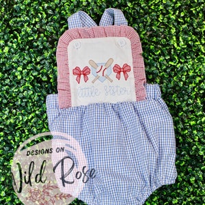 Puede incluir: Un pelele de bebé de vichy azul y blanco con ribetes rojos y blancos. El pelele tiene un panel blanco con lazos rojos bordados, bates de béisbol y una pelota de béisbol. El texto "little sister" está bordado en azul en el panel blanco.