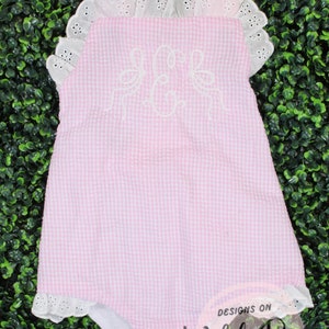 Puede incluir: Un body de beb&eacute; de gingham rosa y blanco con ribete de encaje blanco y un monograma bordado blanco. El body tiene un cuello con volantes y est&aacute; hecho de una tela suave y c&oacute;moda. El body es de Designs on Wild Rose.
