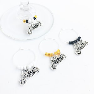 May include: Four silver motorcycle charm wine glass charms. Each charm has a different colored beaded chain: black, white, gold, and yellow.