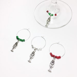 May include: Set of three silver nutcracker wine glass charms. Each charm has a different colored beaded chain: green, white, and red.