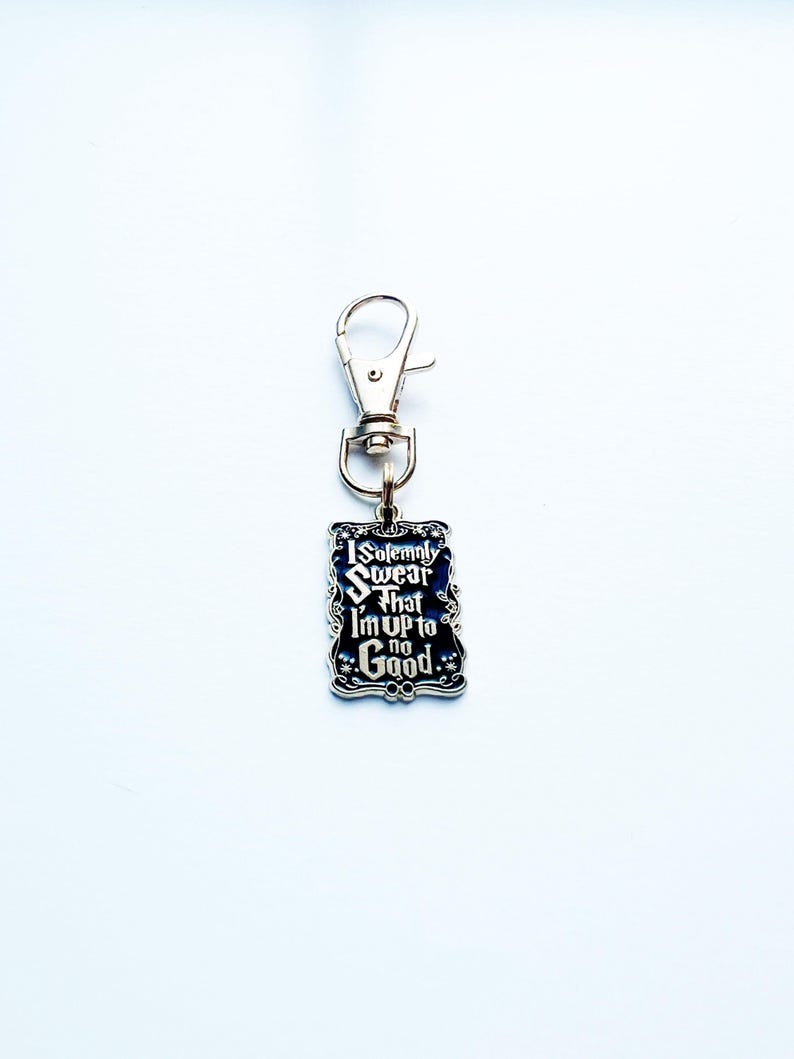 May include: A rectangular keychain with the text "I Solemnly Swear That I'm Up to No Good" in white script on a dark blue background. The keychain has a silver-coloured metal border and a clasp.