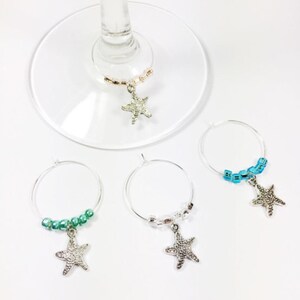 May include: Four silver wine glass charms with starfish charms and colorful beads. The charms are in blue, green, and pink.