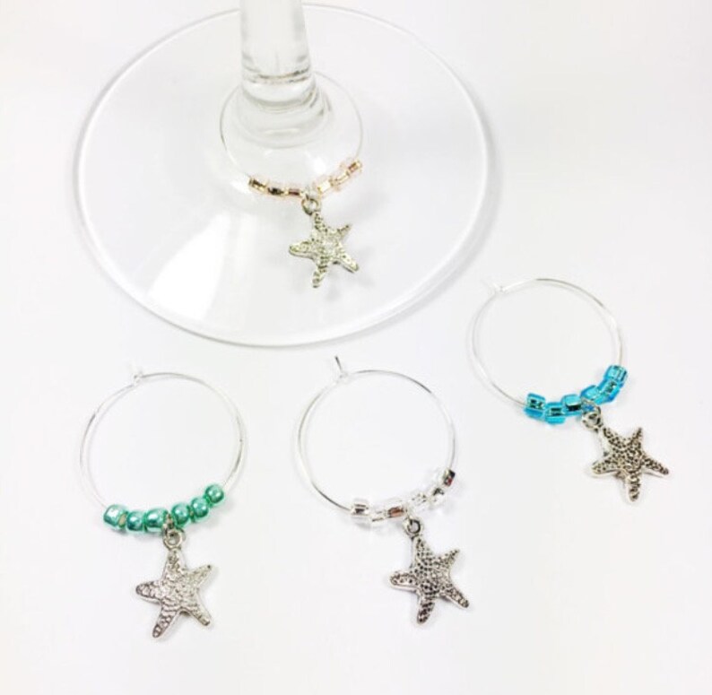 May include: Four silver wine glass charms with starfish charms and colorful beads. The charms are in blue, green, and pink.