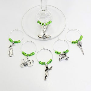 May include: Set of six green and silver golf-themed wine glass charms. Each charm features a different golf-related design, including golf clubs, a golf ball, a golf cart, a golfer, and a golf bag.