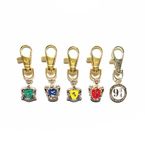 May include: Five gold keychains with different charms. The charms are Hogwarts house crests: Slytherin, Ravenclaw, Hufflepuff, Gryffindor, and a charm with the number "9 3/4" on it.
