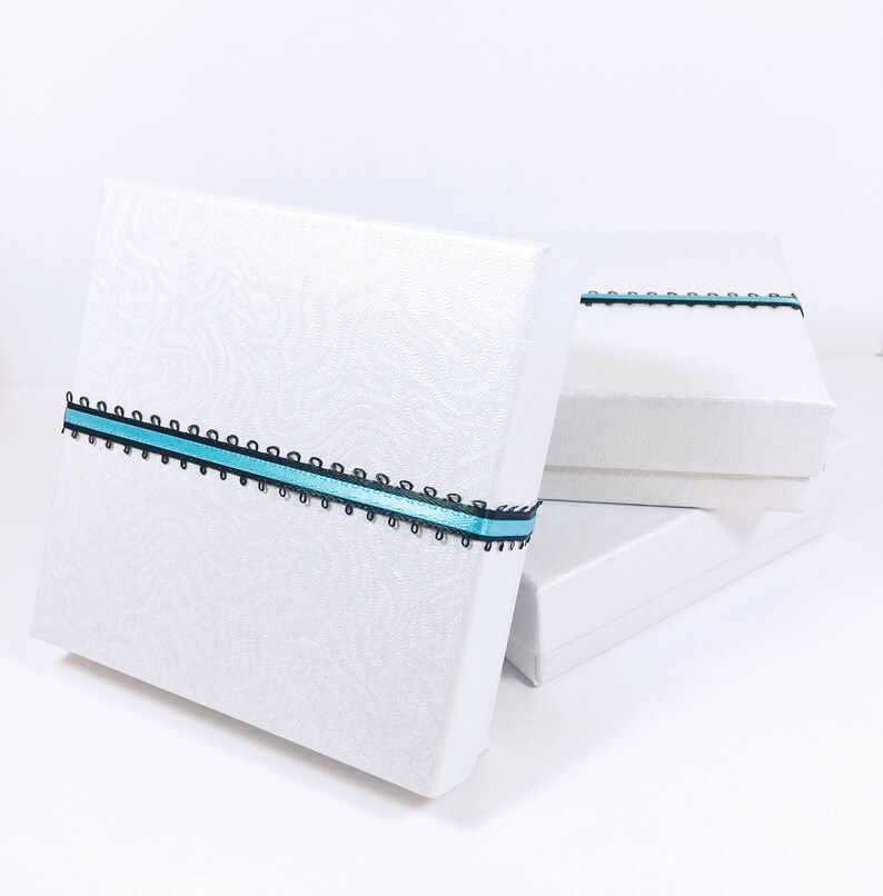 May include: Three white gift boxes stacked on top of each other. The top box has a blue and black ribbon tied around it.
