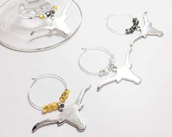 May include: Four silver bull head wine glass charms with different colored beads. The charms are on a white background.