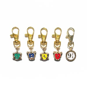 May include: Five gold-toned metal keychains with lobster clasps. Four feature shield-shaped charms with colored enamel centers depicting a snake, bird, lion, and stag. The fifth is a circular charm with the text Platform 9 3/4 King's Cross London.