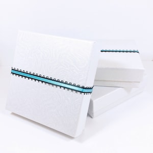 May include: Three white gift boxes stacked on top of each other. The top box has a blue and black ribbon tied around it.