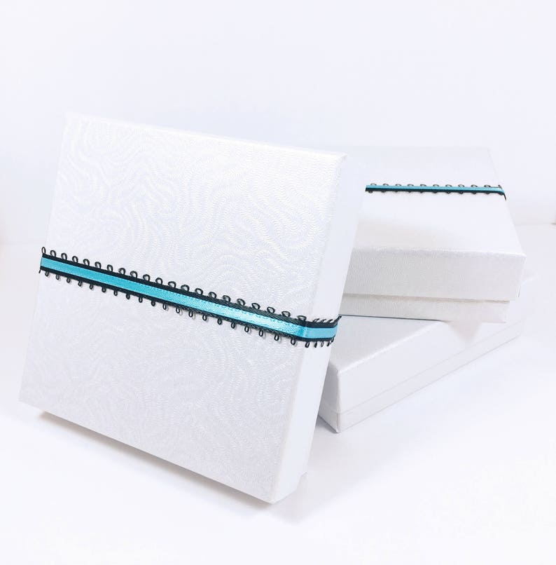 May include: Three white gift boxes stacked on top of each other. The top box has a blue and black ribbon tied around it.