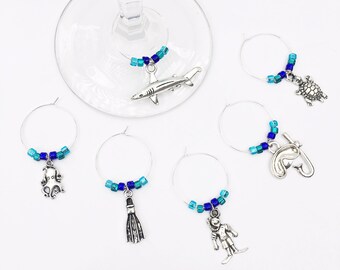May include: Set of six silver wine glass charms with blue and turquoise beads. Each charm features a different sea creature: shark, turtle, octopus, scuba diver, flipper, and a fish with a snorkel.