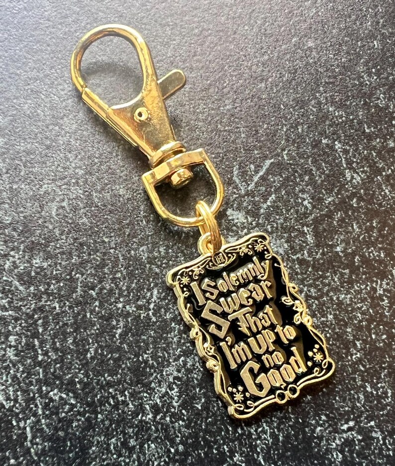 May include: Gold-tone keychain with a lobster clasp and a rectangular charm. The charm features the text "I Solemnly Swear That I'm Up To No Good" on a black background, with gold detailing.