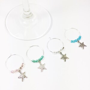 May include: Four silver wine glass charms with beaded chains and starfish pendants. The charms are in shades of blue, green, and pink.