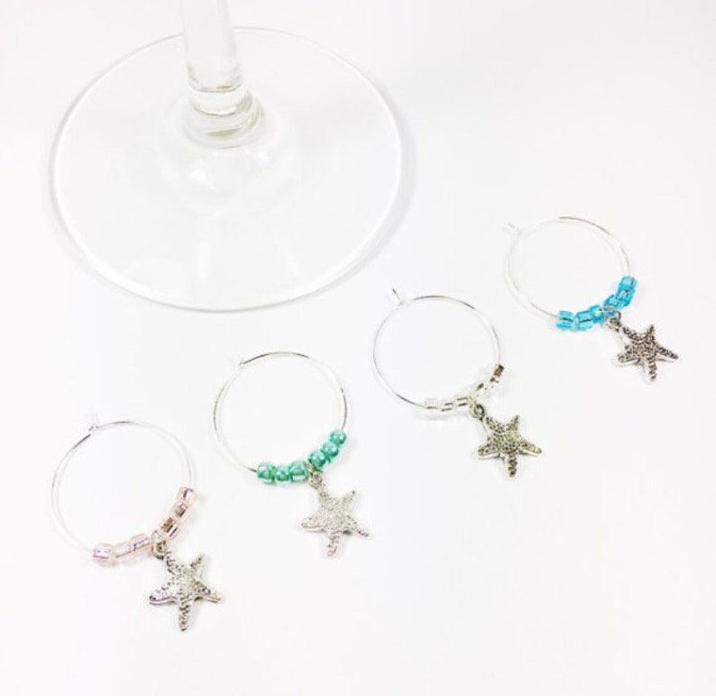 May include: Four silver wine glass charms with beaded chains and starfish pendants. The charms are in shades of blue, green, and pink.