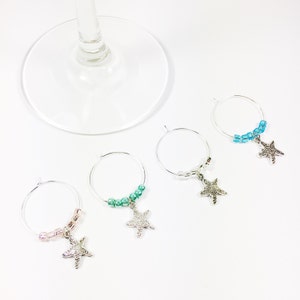 May include: Set of four wine glass charms featuring silver starfish charms with different colored beads. The charms are pink, green, blue, and light blue.
