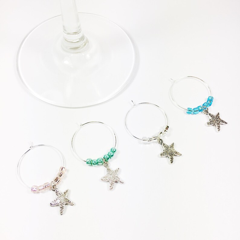 May include: Set of four wine glass charms featuring silver starfish charms with different colored beads. The charms are pink, green, blue, and light blue.