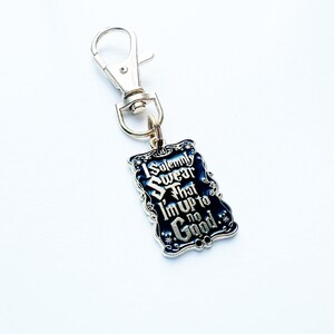 May include: A silver keychain with a rectangular, dark blue charm. The charm features the text "I Solemnly Swear That I'm Up to No Good" in silver lettering. The keychain has a lobster clasp.