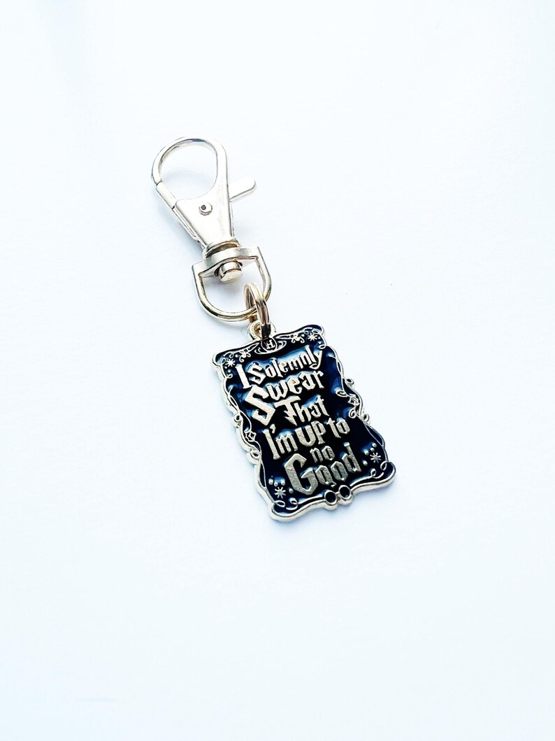 May include: A silver keychain with a rectangular, dark blue charm. The charm features the text "I Solemnly Swear That I'm Up to No Good" in silver lettering. The keychain has a lobster clasp.