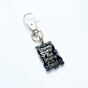 May include: A silver-coloured keychain featuring a rectangular charm. The charm has a black background with the text "I Solemnly Swear That I'm Up to No Good" in white, ornate lettering. The keychain has a lobster clasp.