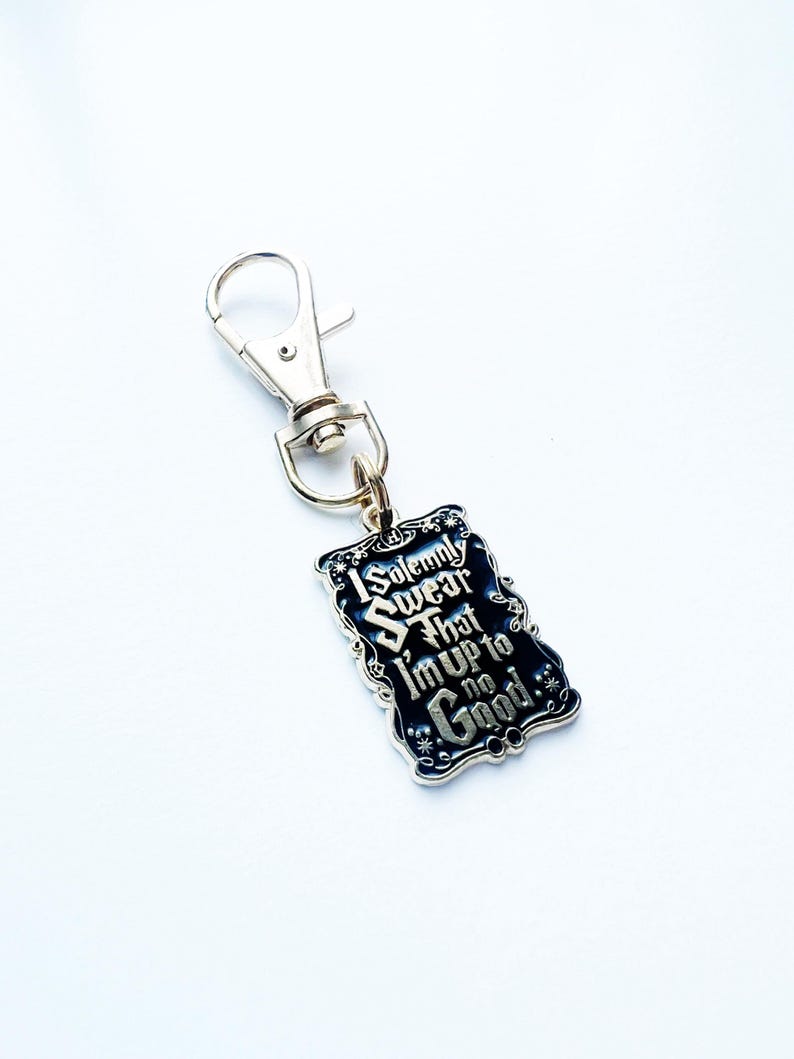 May include: A silver-coloured keychain featuring a rectangular charm. The charm has a black background with the text "I Solemnly Swear That I'm Up to No Good" in white, ornate lettering. The keychain has a lobster clasp.