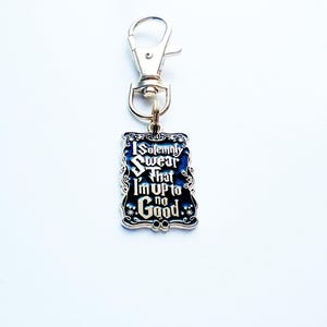 May include: A silver keychain with a rectangular charm. The charm features the text "I Solemnly Swear That I'm Up to No Good" on a black background. The charm is edged in silver with decorative flourishes.